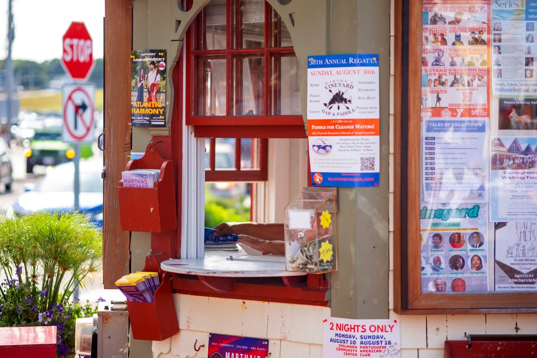 The Oak Bluffs information booth by the harbor, its window layered with posters for island events. B...