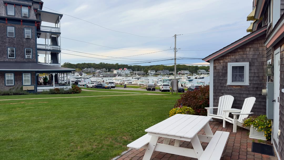 A quiet spot by Oak Bluffs Harbor, a picnic table and Adirondack chairs on the lawn, cedar-shingled...