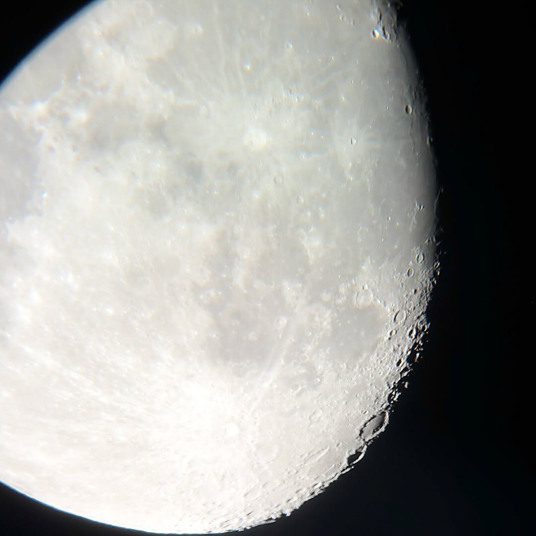 A gibbous Moon through a telescope eyepiece, shot with a phone held up to the lens. The craters show...