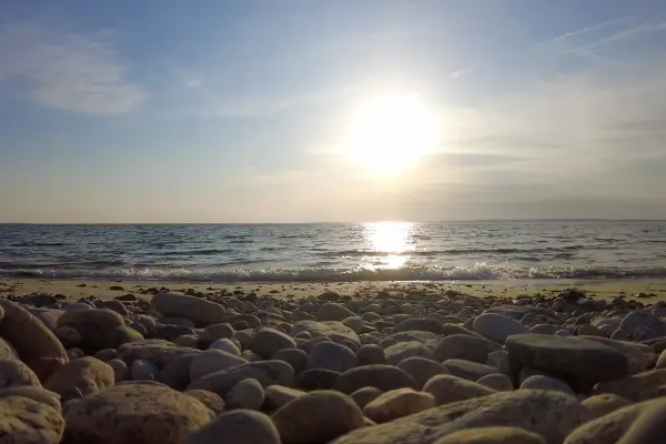 Low sun shining over the surf from a pebbly beach